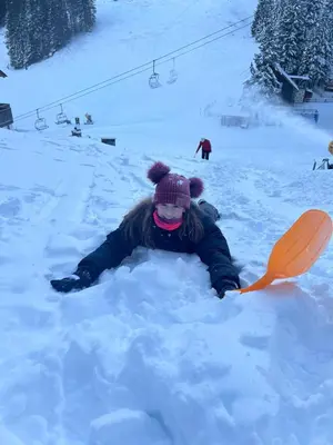 a woman laying in the snow with an orange shovel at Apartma Lilija Golte in Mozirje