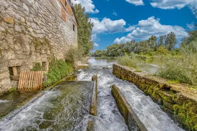 a river next to a stone wall with waterfalls at River View Suite Mlinar Private Beach - Happy Rentals in Metlika