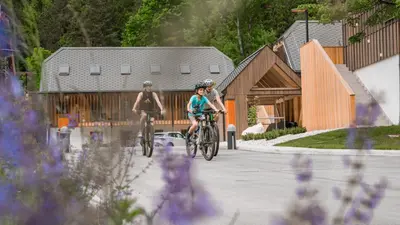 two people riding bikes in front of a building at Residence Soča in Soča