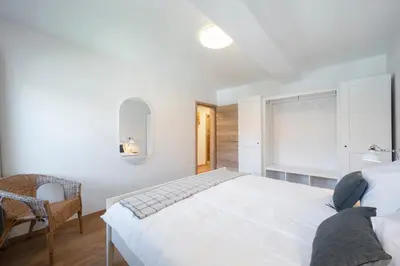 a white bedroom with a bed and a chair at GrosAlp apartments in Lesce