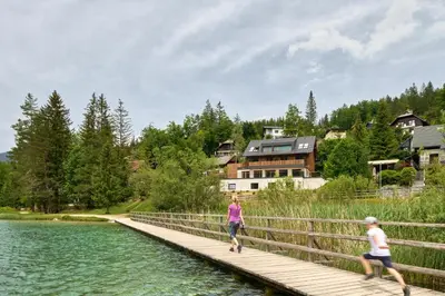 two people walking across a wooden bridge over a lake at Milka Boutique Hotel in Kranjska Gora