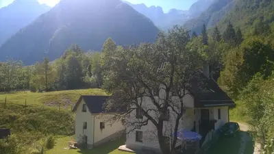 a house in a field with mountains in the background at Apartment Pretner, Lepena in Soča