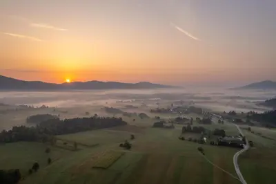 a foggy sunrise over a field with the sun rising in the background at Glamping Happiness - Natural Pool & Wellness in Ribnica