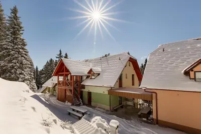 a house covered in snow with the sun in the sky at Apartma Valsar Rogla in Zreče