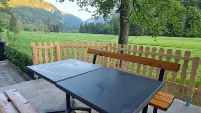 a wooden bench with a table in front of a field at Radovna Mountain Valley Cottage in Zgornje Gorje