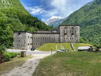 a large stone building with cars parked in front of a mountain at Apartment 3 Sovice in Bovec
