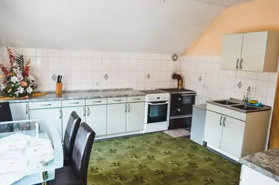 a kitchen with white cabinets and a table with chairs at Apartmaji Krebs in Mežica