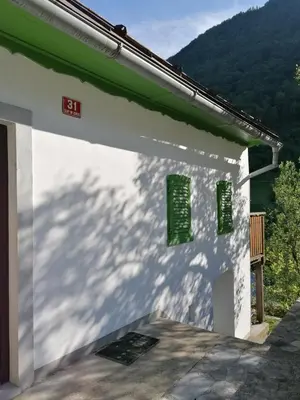 a white building with green windows on the side at počitniška hiška MEDVEJKE in Slappe dʼIdria