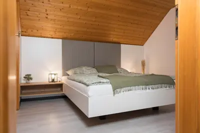 a bedroom with a white bed with a wooden ceiling at Hiša Rodica in Bohinj