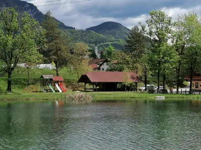 a cabin next to a lake with mountains in the background at Lahova hiša in Ljubno