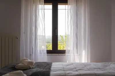 a bedroom with a bed with white curtains and a window at Apartma ODDIH in Dutovlje
