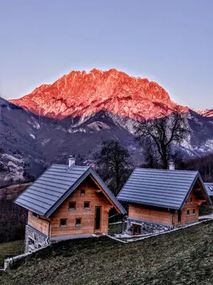 two houses on a hill with a mountain in the background at Granaries Pear & Walnut in Tolmin
