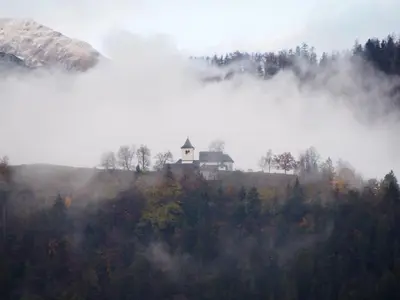 a house on top of a hill in the fog at Tony's Old Farm in Begunje na Gorenjskem