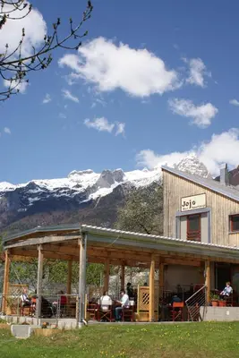 a building with people sitting at tables in front of a mountain at Apartments Jojo in Bovec