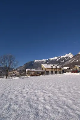 a snow covered field with a building and mountains at Apartments Jojo in Bovec