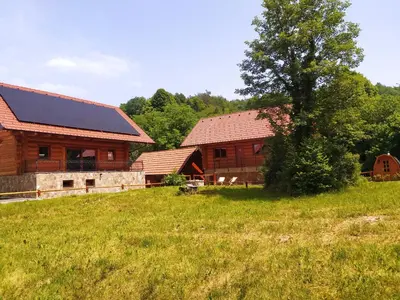 a barn with a house and a tree in a field at Brunarica Biopark -Log house Biopark in Grosuplje