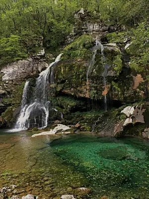 a waterfall and a pool of emerald green water at Pri Zajcu in Bovec