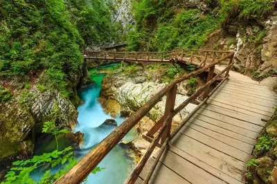 a wooden bridge over a river with blue water at Zemva Stays - Apartma ELA in Zgornje Gorje