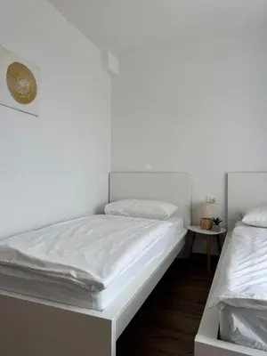 a white bedroom with two beds and a table at Apartment ZEN in Zgornje Škofije