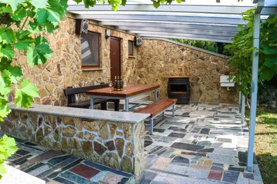 a patio with two benches and a stone wall at Počitniška hiška pod Hadikom in Lendava