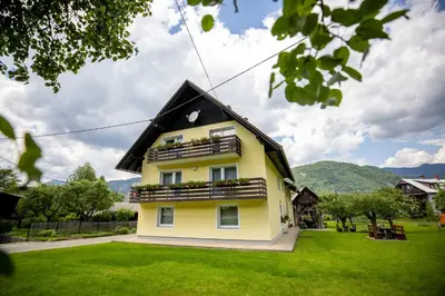 a yellow house with balconies on a green yard at Apartmaji Arh Matilda in Bohinj