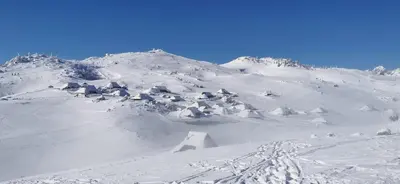 a mountain covered in snow with a bunch of buildings at Koča Pastirica - Velika planina in Stahovica