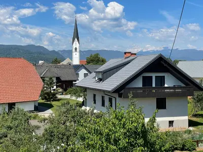 a white house with a church with a steeple at ANMARI Apartment & Rooms in Radovljica