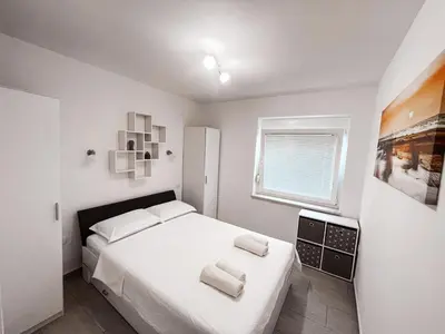 a white bedroom with a bed and a window at RIAD Apartments in Zgornje Škofije