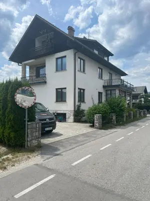 a white house with a car parked on the side of the road at Apartmaji Iva in Bled