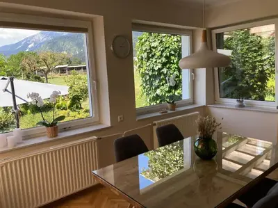 a dining room with a glass table and three windows at Vila Mir - Apartment in Begunje na Gorenjskem