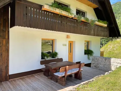 a house with a wooden deck with a table and benches at Apartma Korošec in Srednja Vas v Bohinju