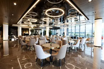 a restaurant with white chairs and tables and windows at Grand Plaza Hotel & Congress Center in Ljubljana