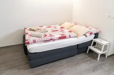 a small bed with a red and white blanket and a stool at Apartma pri lipi in Bohinj