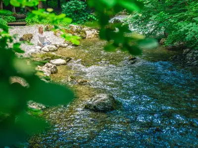 a woman sitting on the rocks next to a stream at Garden Village Bled in Bled