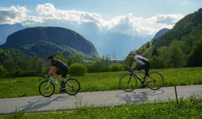 two people riding bikes down a road with mountains in the background at Chalet Hike&Bike above Bohinj valley in Bohinj