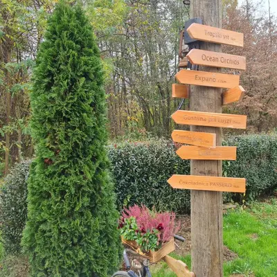 a directional sign in a garden next to a tree at Gozdarjeva hiška M&K in Dobrovnik