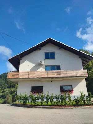 a white house with a balcony on top of it at Apartments and rooms pri Bašlju in Cerkno