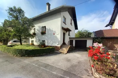 a white house with flowers in a driveway at Rooms Apartma Cerknica in Cerknica
