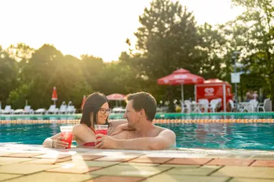 a man and woman in a swimming pool with drinks at Thermal Resort Hotel Lendava in Lendava