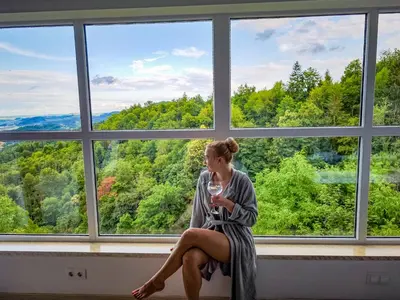 a woman sitting in a window with a glass of wine at Private wellness with panoramic view, sauna & jacuzzi in Maribor