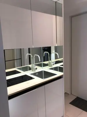 a kitchen with white cabinets with sinks and mirrors at Sunny home with cute dragon in the center+parking in Ljubljana