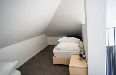 a small white room with a bed and pillows at Villa Magdalena apartments & rooms GARNI HOTEL in Maribor