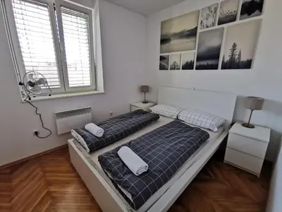 two beds in a white room with two windows at Apartment for four with free parking in Ljubljana