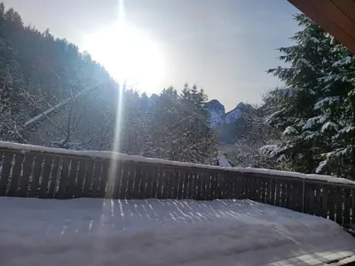 a snow covered deck with the sun shining through the trees at Apartma Modro gnezdo in Kranjska Gora