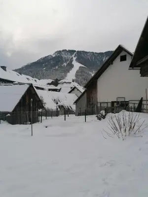 a snow covered field with a barn and mountains at Apartma Tilika in Kranjska Gora