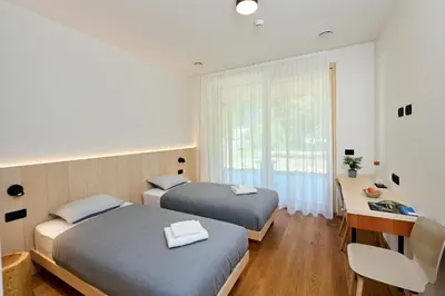 two beds in a room with a desk and a window at Na trati Pension in Črna na Koroškem