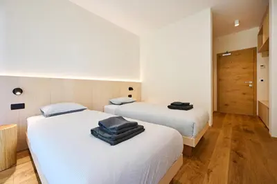 two beds in a room with white walls and wooden floors at Na trati Pension in Črna na Koroškem
