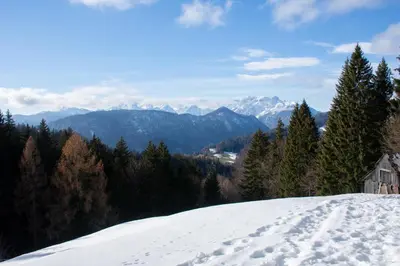 a snow covered hill with a house and mountains in the background at Alpine Cottage Golica in Jesenice