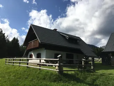 a small house with a wooden fence in a field at Apartma Hodnik Bohinj Uskovnica in Srednja Vas v Bohinju