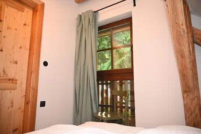 a bedroom with a bed and a window with a chair at SLO-ETNO HOUSE GOSTECE-Vintage Apartma in Mozirje